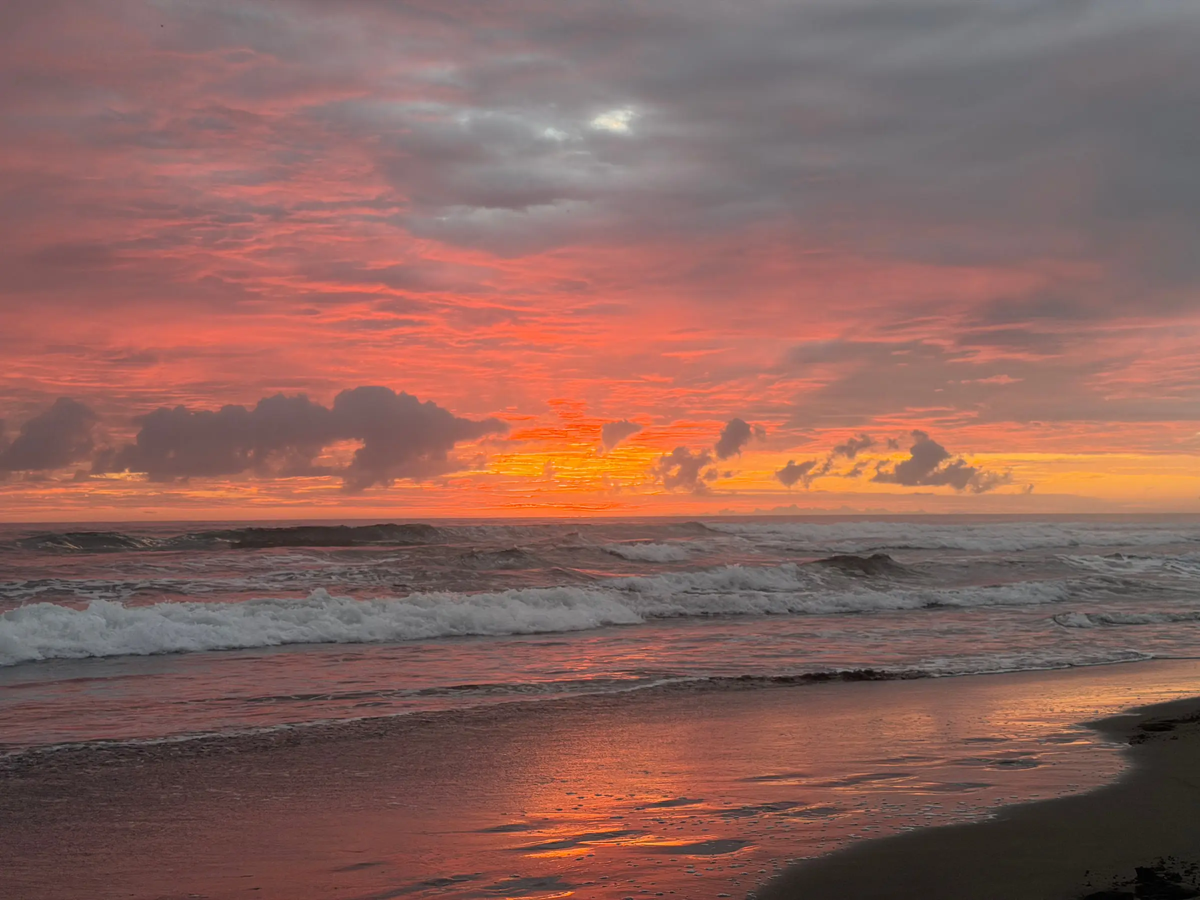 Sunset over the Pacific from the beach, the wet sand holding the color of the sky