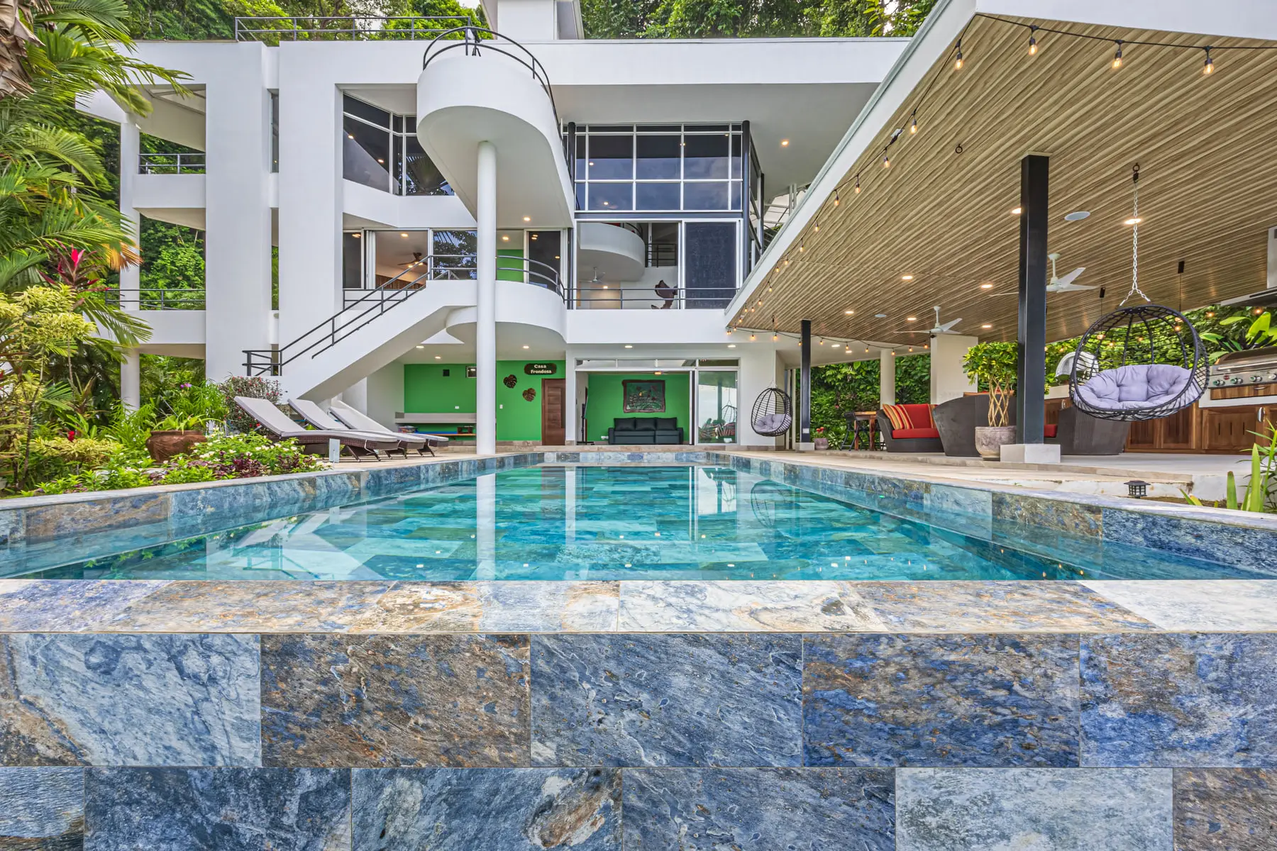 The house seen from the pool terrace, its curved staircase and glass wall open to the jungle